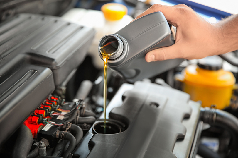 Mechanic pouring oil into car engine, closeup