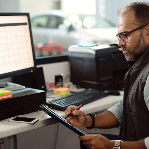 Auto mechanic analyzing reports while working on desktop PC in the office.